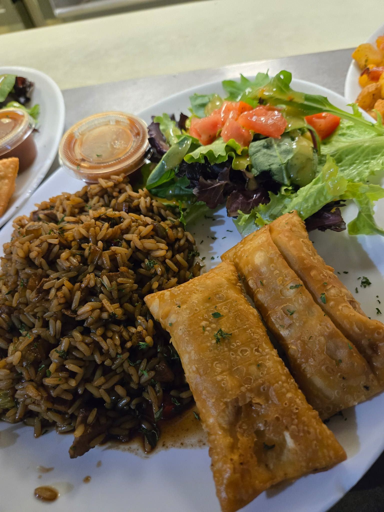 Une assiette composée de riz noir assaisonné, de deux petits pains frits dorés, d'une salade d'accompagnement avec vinaigrette et d'une petite sauce.