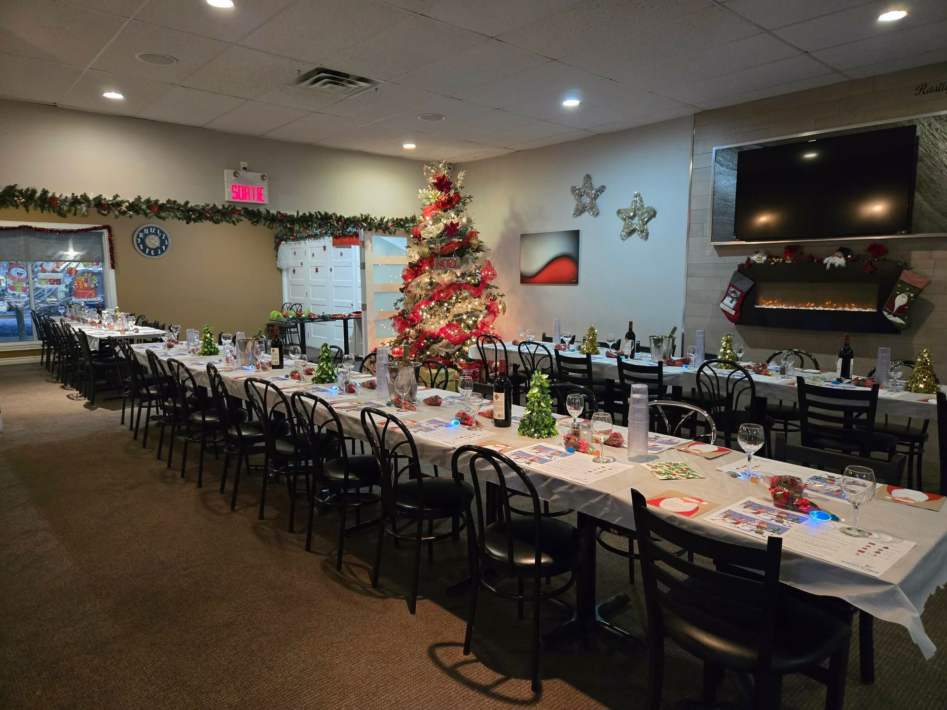 Une salle décorée pour une fête, avec de longues tables, des chaises, des décorations de Noël et un sapin décoré.