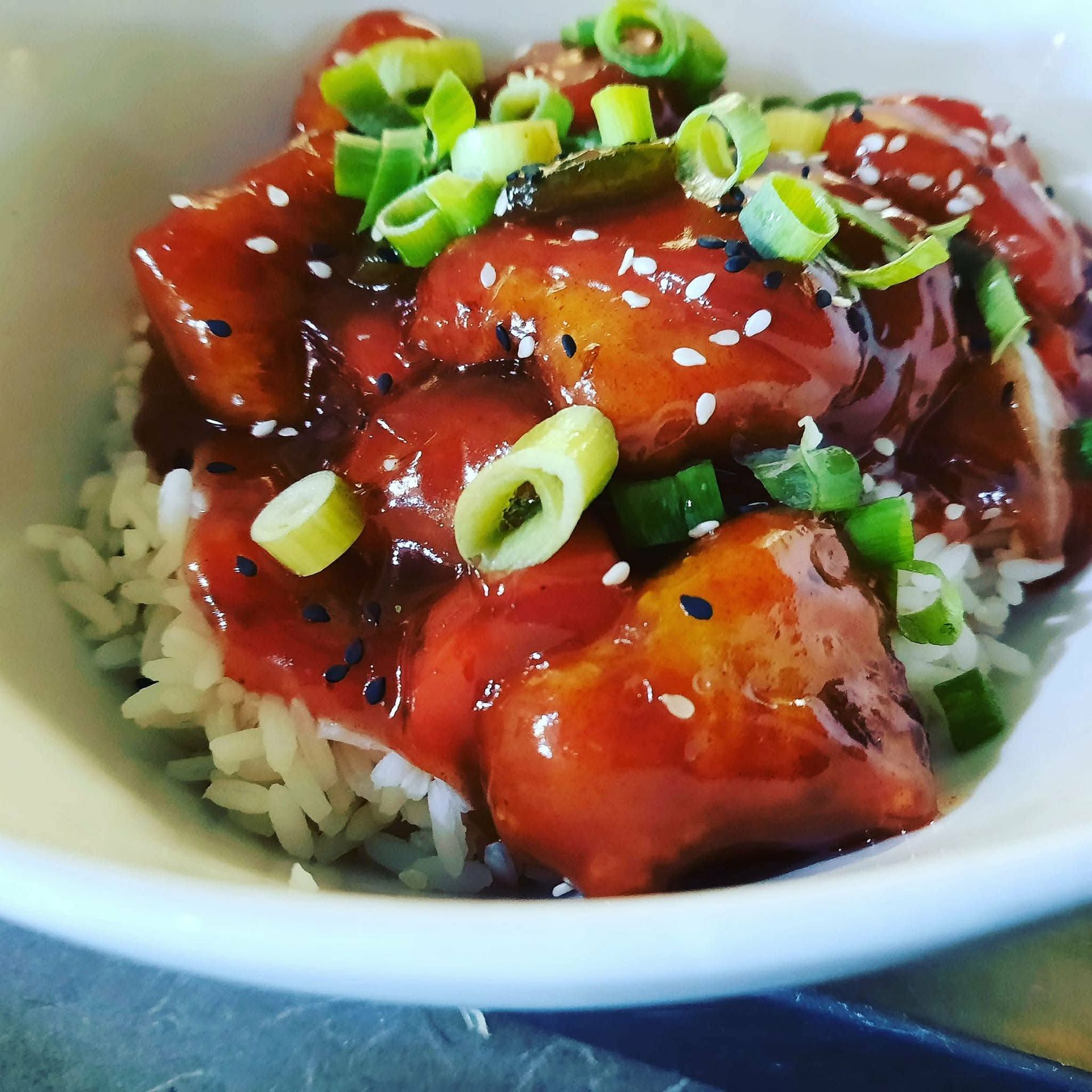 Poulet glacé servi sur du riz blanc dans un bol, garni d'oignons verts émincés et de graines de sésame