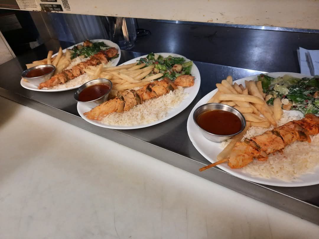 Trois assiettes de brochettes de poulet, des frites, du riz et une sauce à côté étaient alignées sur le comptoir d'un restaurant.