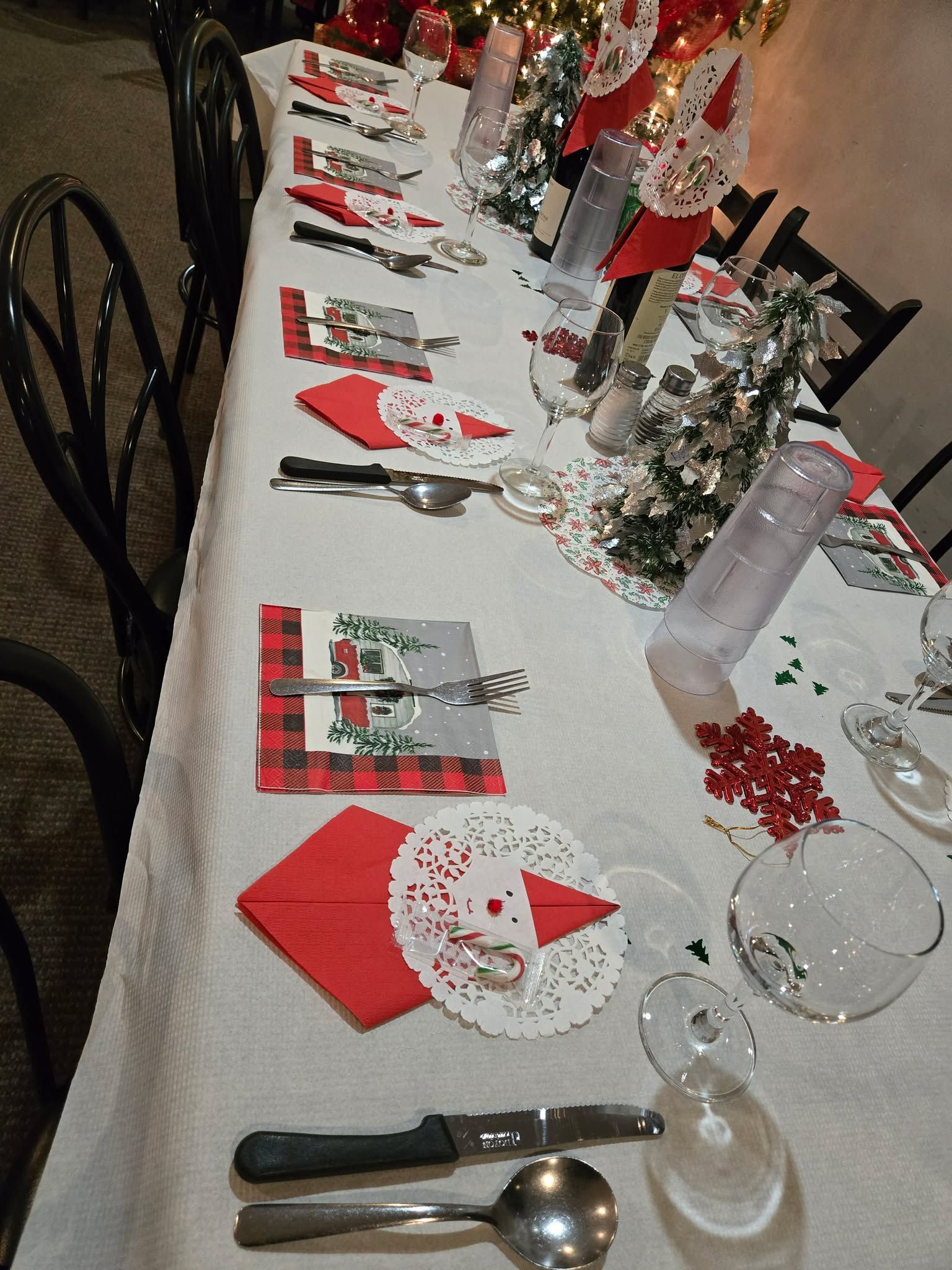 Une longue table dressée pour un repas de fête, avec des serviettes rouges, des napperons en dentelle blanche, des couverts et des centres de table décoratifs.