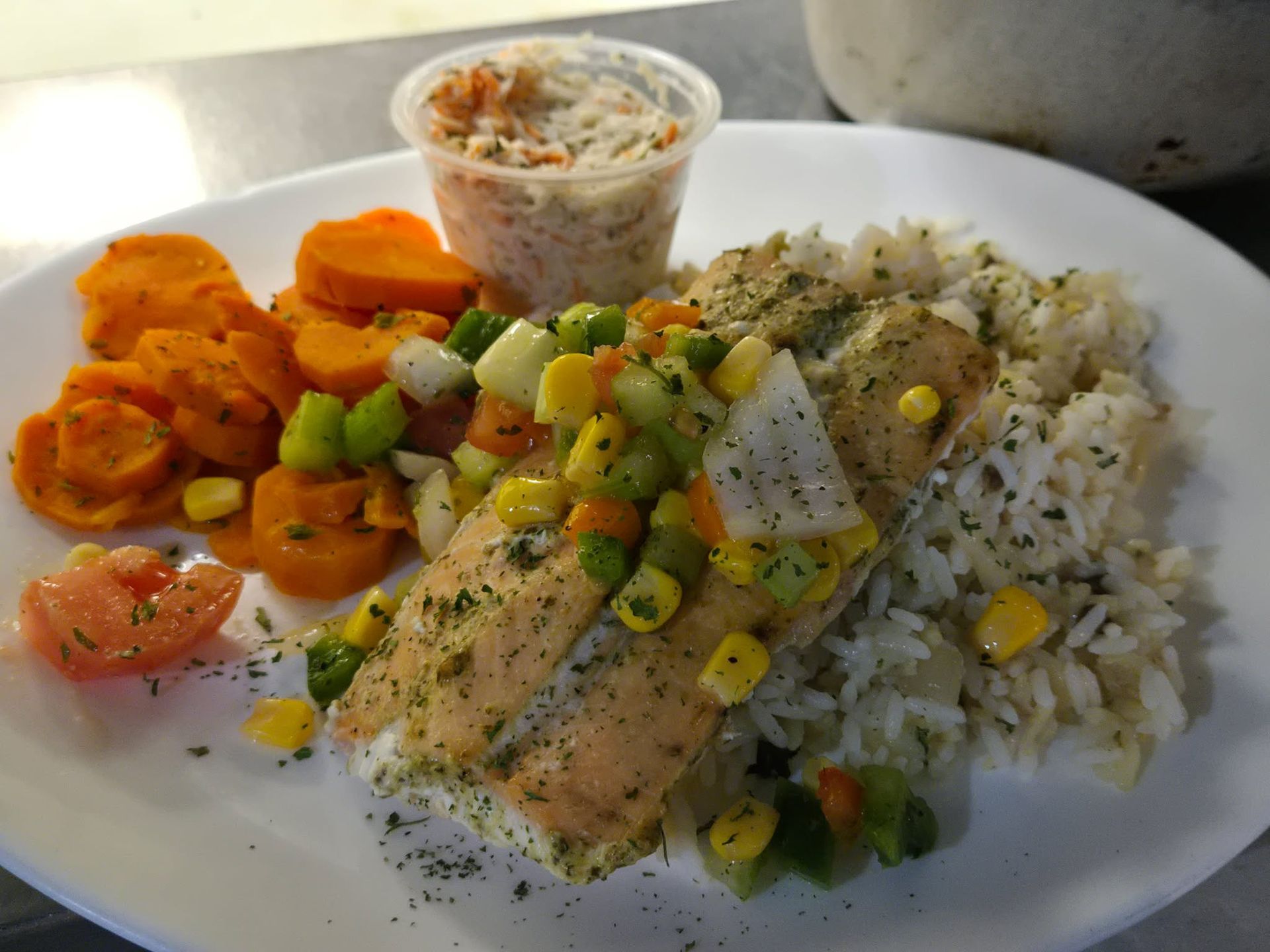 Saumon servi avec du riz, des carottes et des légumes variés, accompagné d'une petite portion de salade de chou.