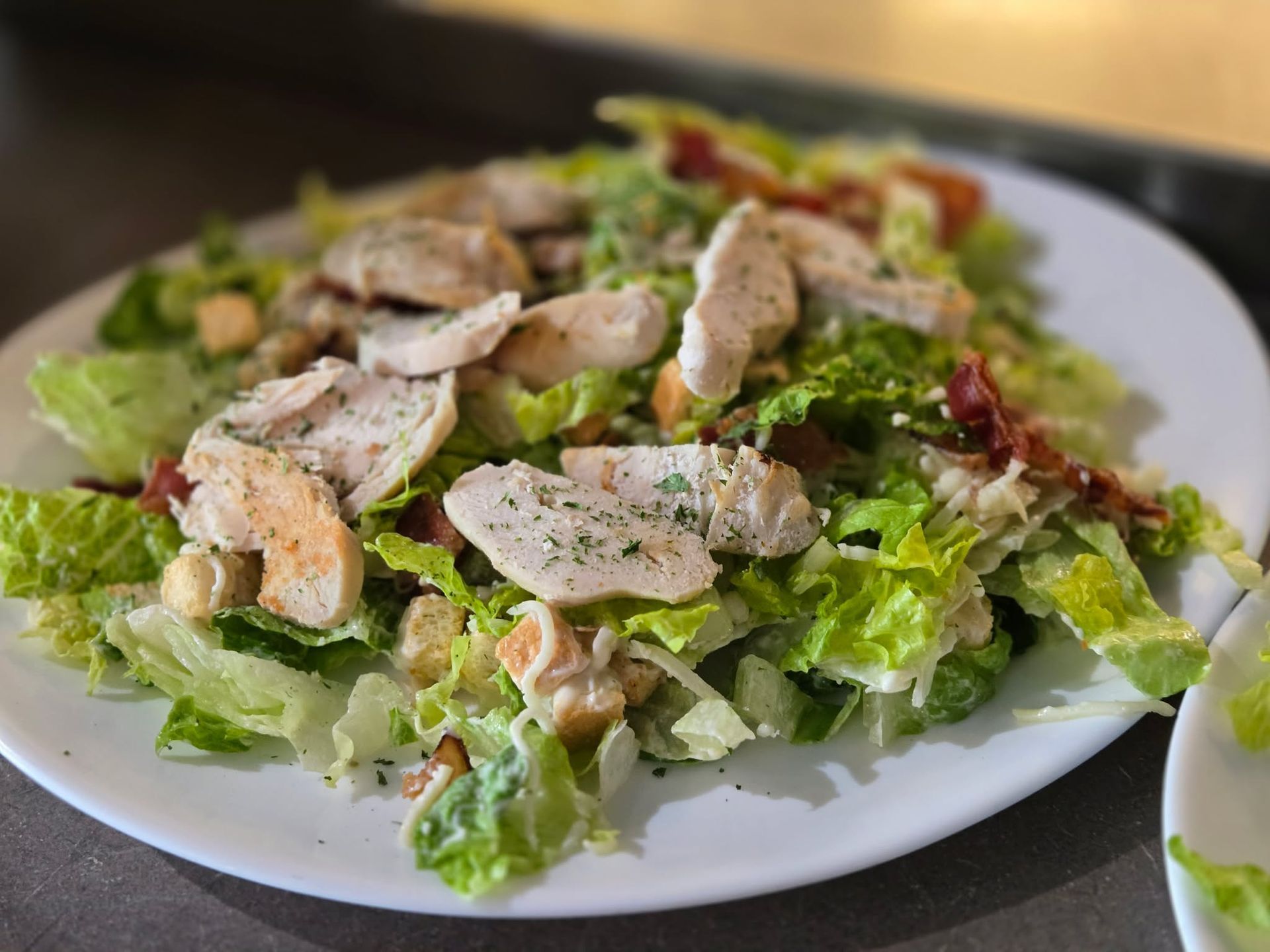 Une assiette de salade César garnie de tranches de blanc de poulet grillé, de croûtons et de morceaux de bacon.