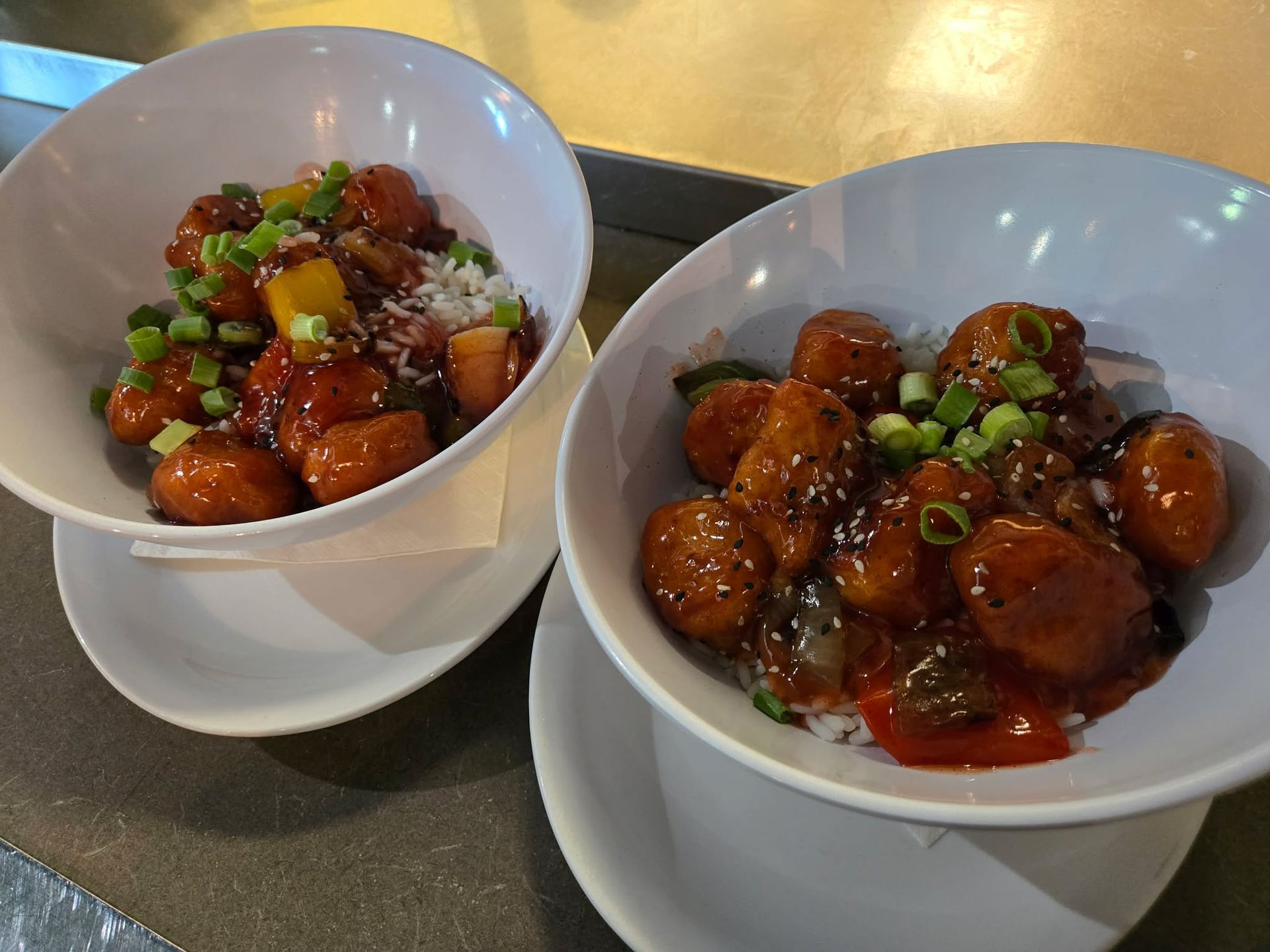 Deux bols de poulet glacé aux oignons verts, présentés sur des assiettes blanches et servis sur une table.