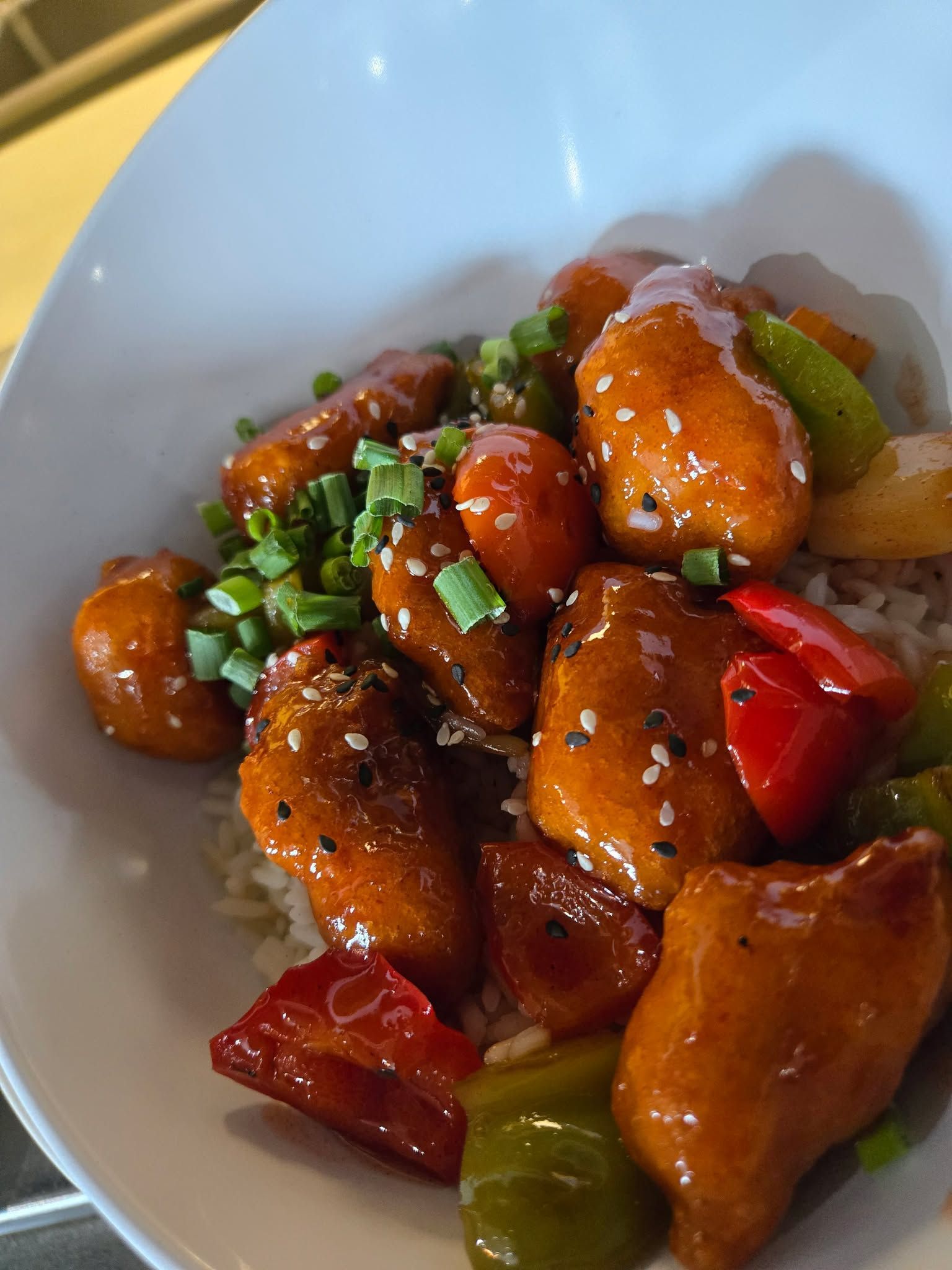 Un bol de poulet aigre-doux glacé avec des poivrons et des oignons verts, servi sur du riz blanc.
