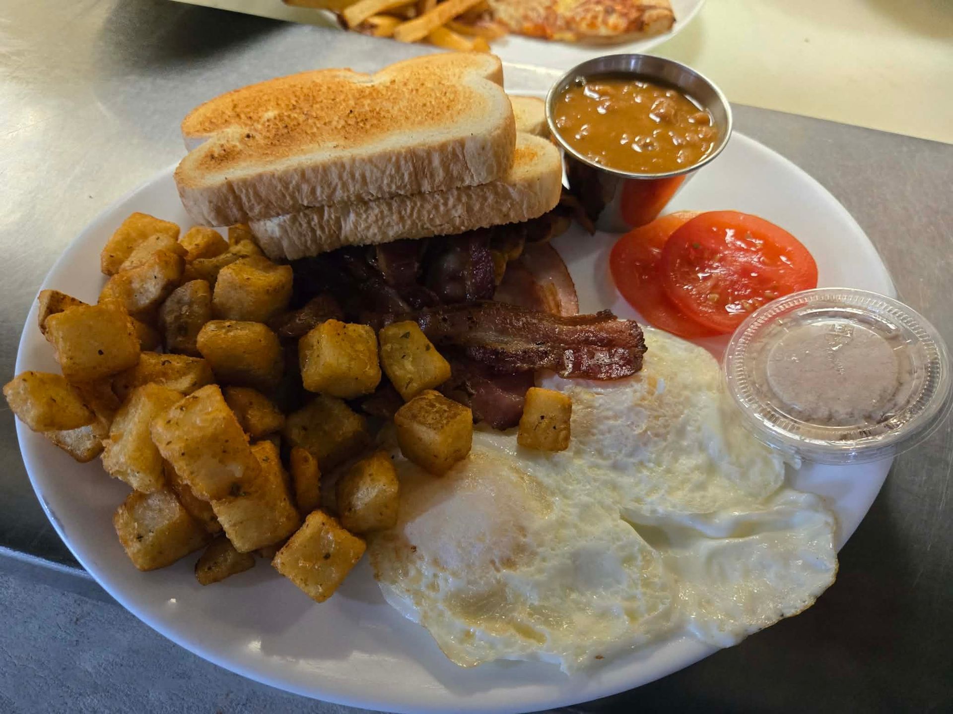 Assiette de petit-déjeuner avec toasts, pommes de terre, bacon, œufs au plat, tranches de tomates et sauce.