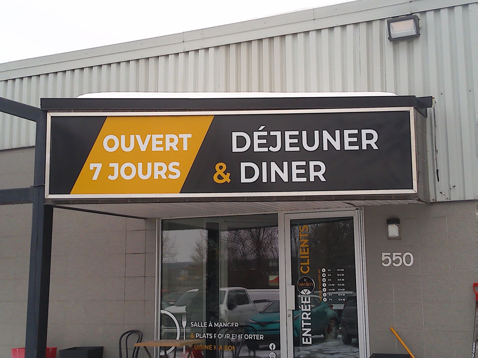 Extérieur d'un restaurant avec une enseigne indiquant « OUVERT 7 JOURS » et « DÉJEUNER & DINER » au-dessus d'une porte d'entrée vitrée.