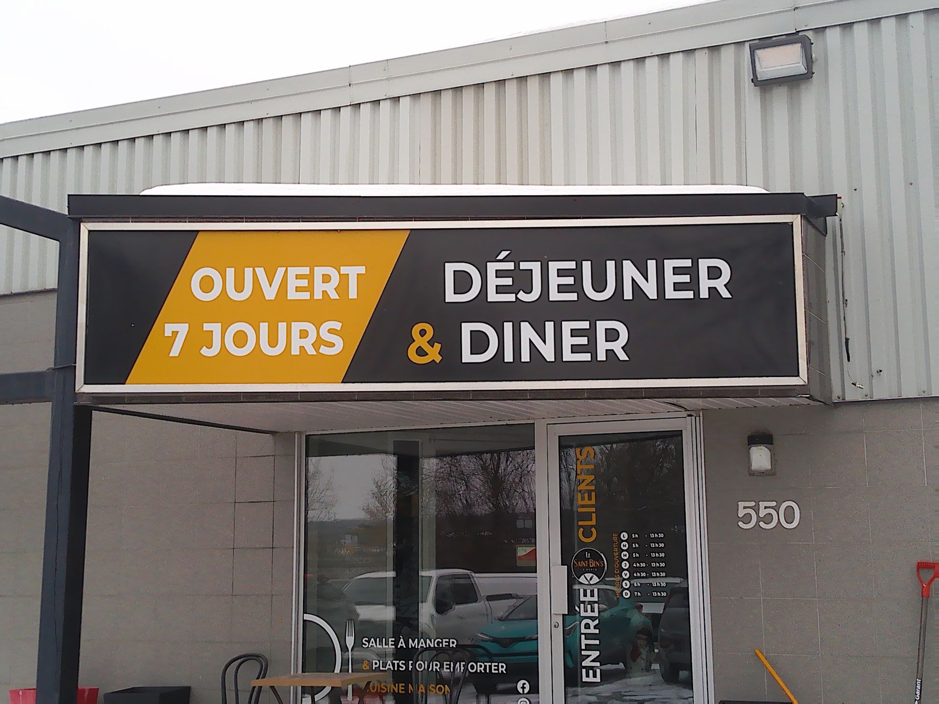 Une enseigne de restaurant indique « OUVERT 7 JOURS » (Ouvert 7 jours) et « DÉJEUNER & DINER » (Petit-déjeuner et dîner) au-dessus d'une entrée vitrée.