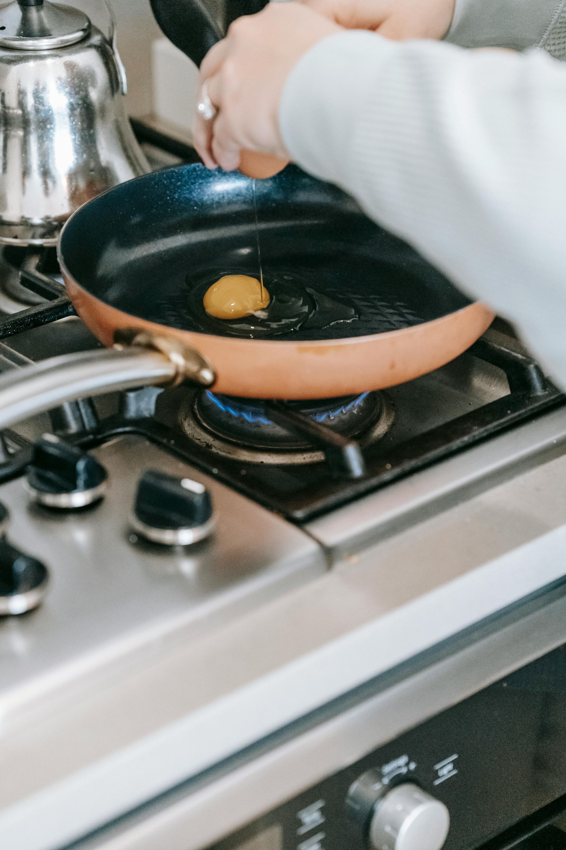 Une personne casse un œuf dans une poêle à frire couleur cuivre sur une plaque de cuisson à gaz.