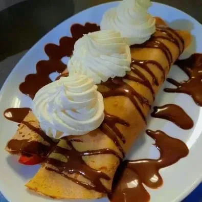 Crêpe dessert nappée de chocolat et garnie de crème fouettée, servie sur une assiette blanche.