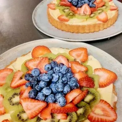 Deux tartelettes aux fruits garnies de fraises, de kiwis et de myrtilles tranchés, présentées sur des assiettes rondes.