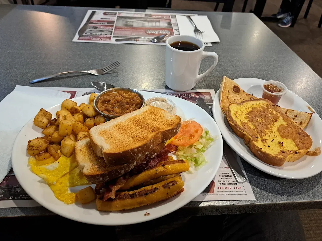 Un repas de type «diner» comprenant un sandwich au bacon, des pommes de terre rissolées, une petite coupelle de sauce, un café et du pain perdu en accompagnement.