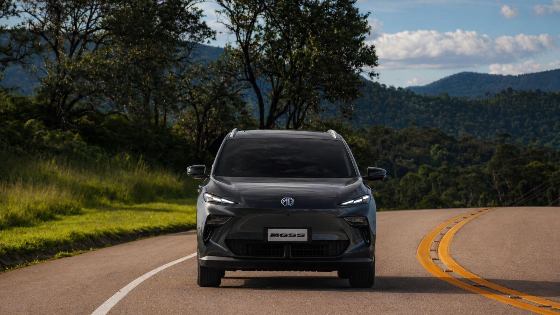 Black SUV driving on a curving country road with trees and hills in the background