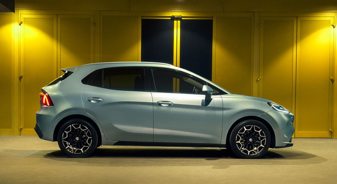 Carro hatchback prateado estacionado de lado em uma garagem ou showroom com iluminação amarela.