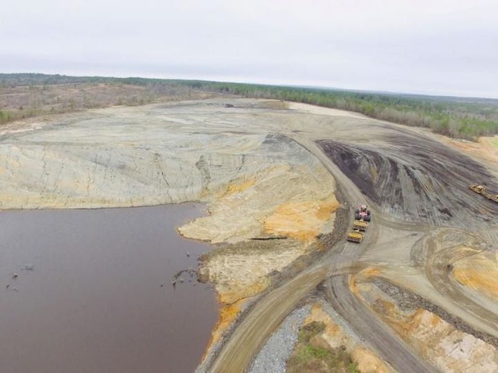 Aerial view of an open-pit mine with muddy water, pale rock slopes, and haul trucks on a dirt road