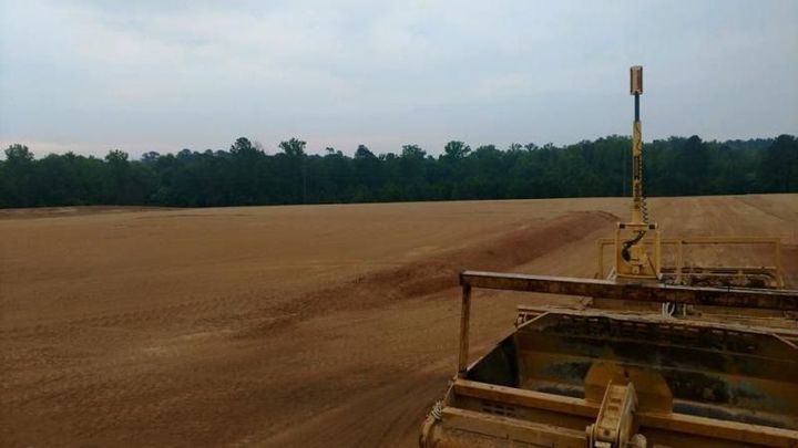 Farm field viewed from a tractor, with brown soil and a tree line under an overcast sky.