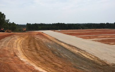Dirt road beside a long concrete strip at a cleared construction site under a cloudy sky