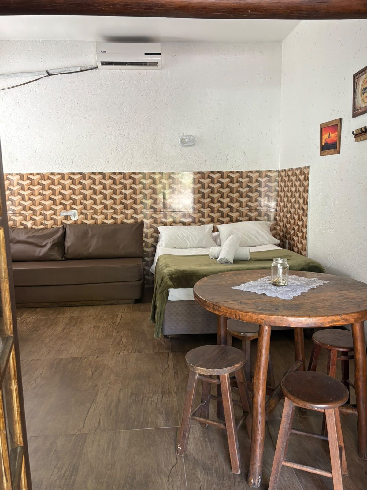Sala de estar pequena com sofá, cama, mesa redonda de madeira e bancos sobre o piso de azulejos