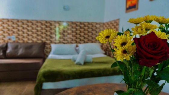Quarto com cama e sofá, com um buquê de flores amarelas e vermelhas em primeiro plano