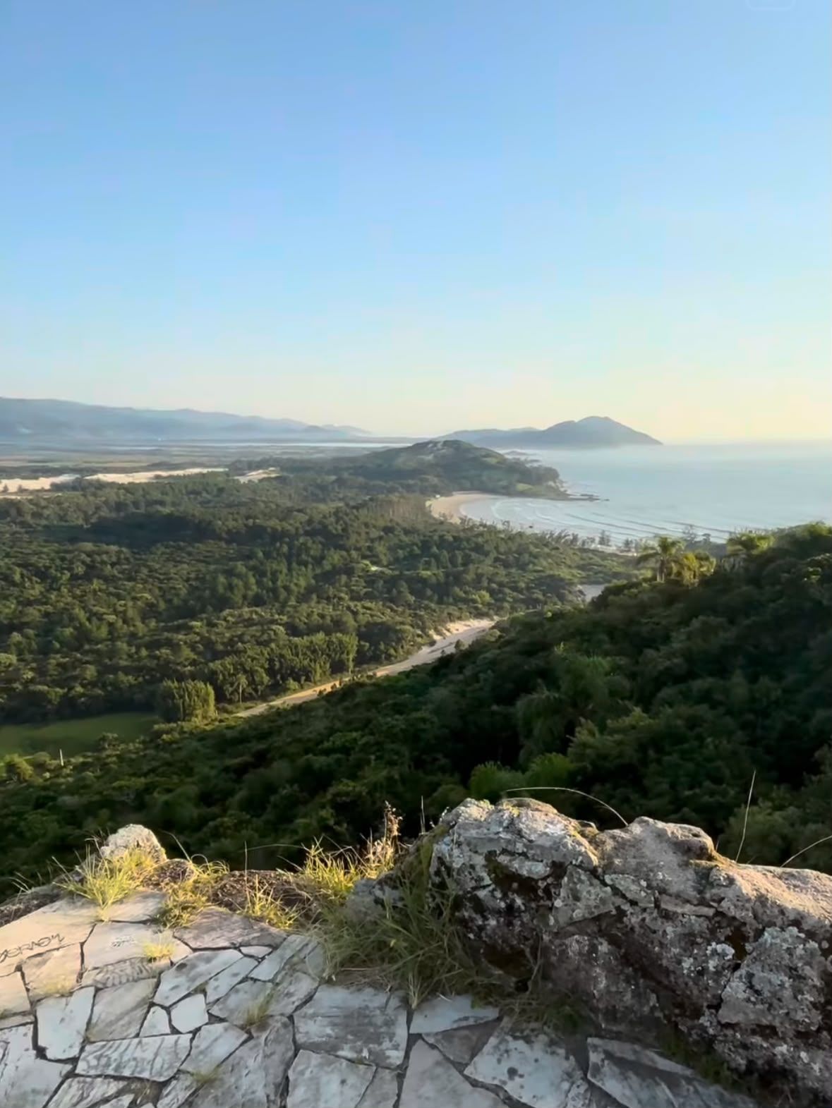 Miradouro rochoso sobre uma costa verdejante e um mar azul sob um céu limpo