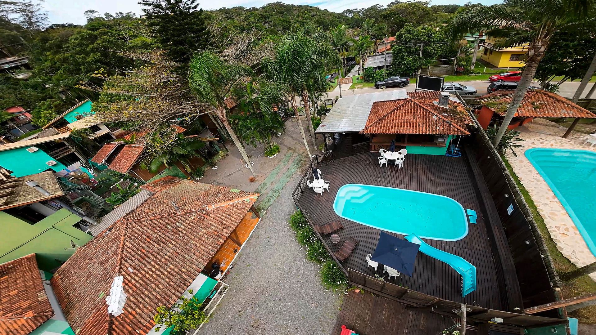Vista aérea de um resort tropical com piscina, cabanas, palmeiras e um caminho sinuoso