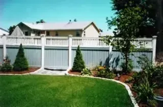 Backyard with green lawn, white fence, and landscaped garden under a clear blue sky