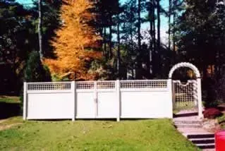 White fence and garden gate in a grassy yard with trees in the background
