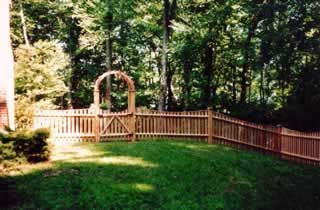 Wooden garden fence with an arched gate in a wooded backyard lawn