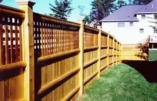 Wooden lattice fence lining a green backyard beside a house under clear blue sky