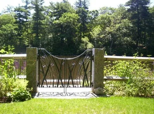Decorative metal gate between stone pillars in a sunny garden with green lawn and trees