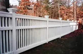 White vinyl fence along a yard with autumn trees in the background