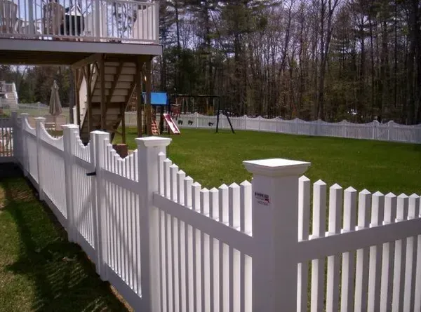 White vinyl fence bordering a green backyard with a deck and wooded yard beyond