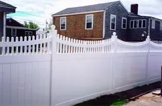 White vinyl picket fence with decorative arched top in front of a house and driveway