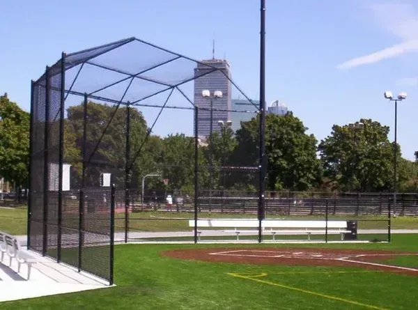 Baseball field with a netted batting cage, green grass, and a clock tower in the background