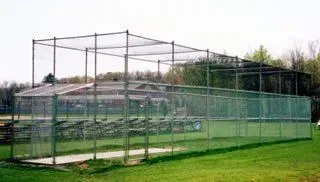 Large outdoor batting cage with green netting and metal frame on a grassy field