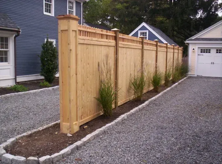 New wooden privacy fence along a gravel driveway beside houses