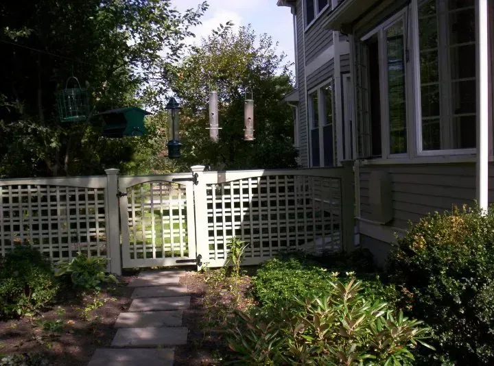 White lattice gate beside a gray house and garden path under bright sunlight