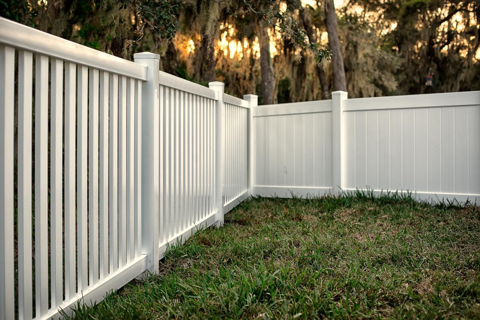 White vinyl fence enclosing a grassy yard with trees in the background