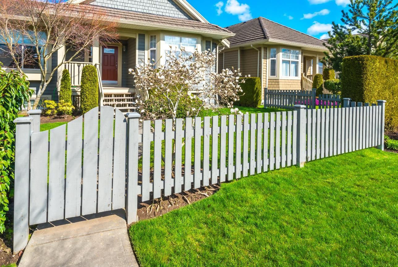White picket fence along a green lawn in front of a suburban house