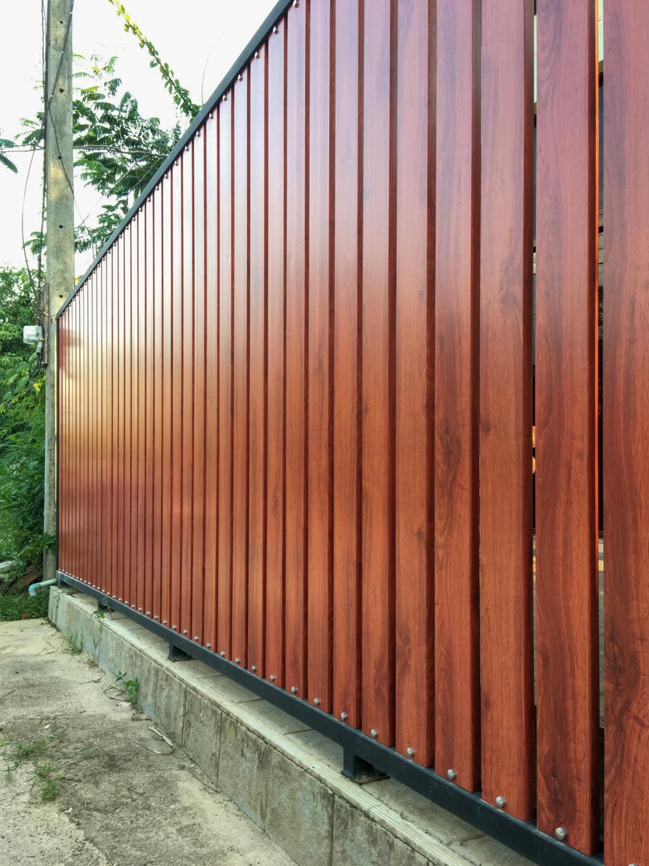 Long red wooden fence along a concrete base beside a narrow path and green trees