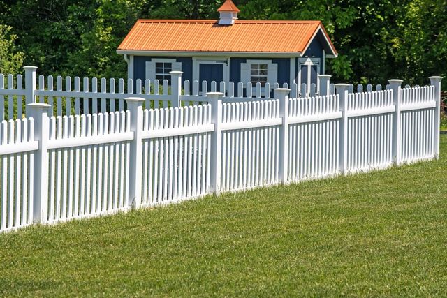 White picket fence in front of a small house with an orange roof on a grassy lawn