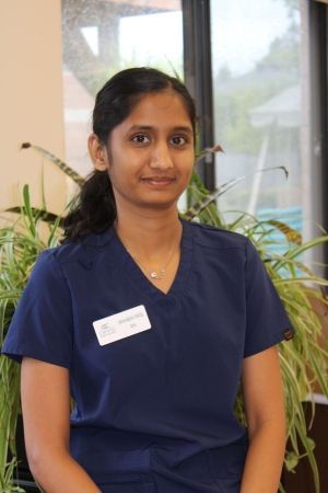 Person in navy scrubs standing indoors with a name badge and a slight smile.