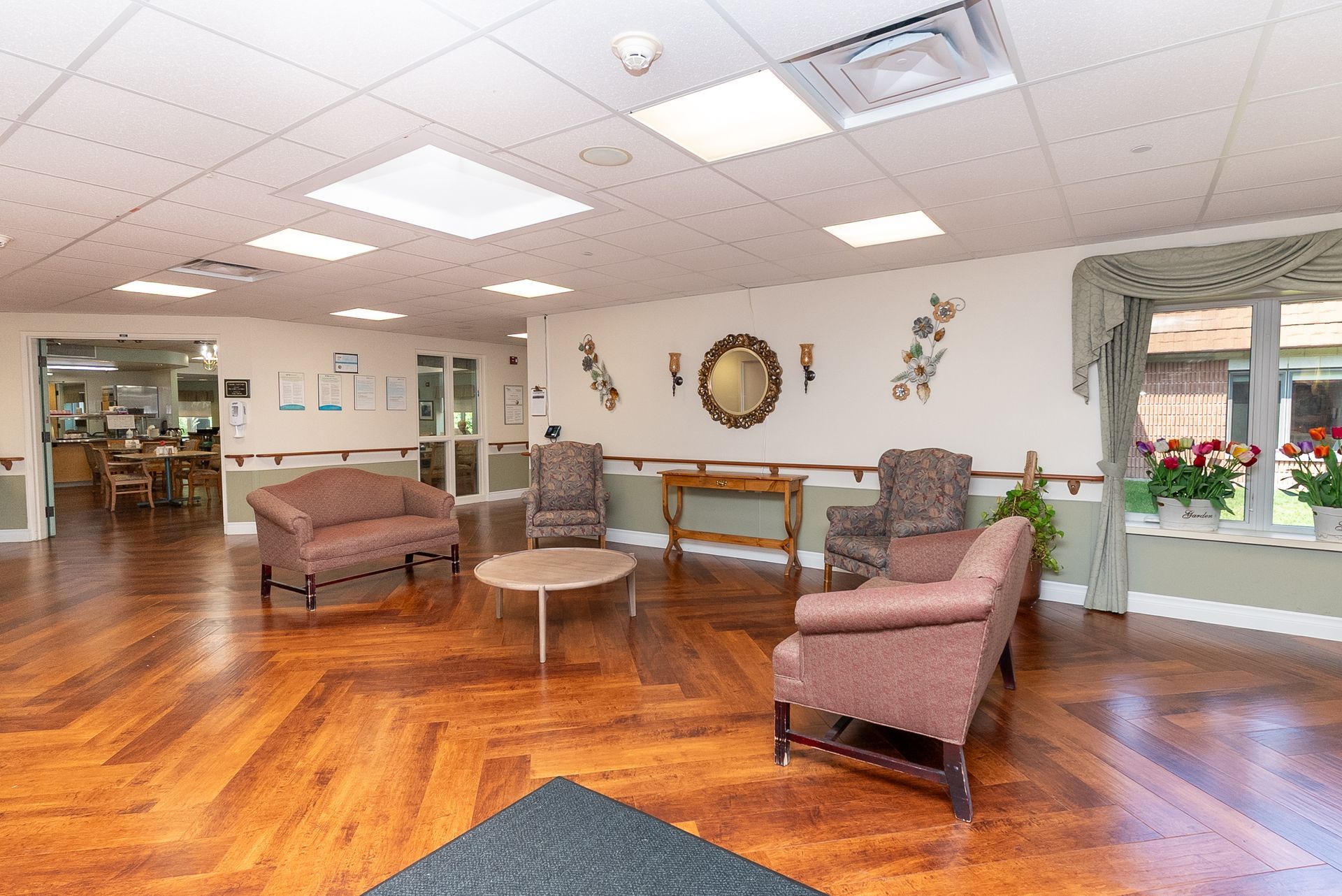 Bright lobby with polished wood floors, mauve chairs, tables, and a windowed waiting area