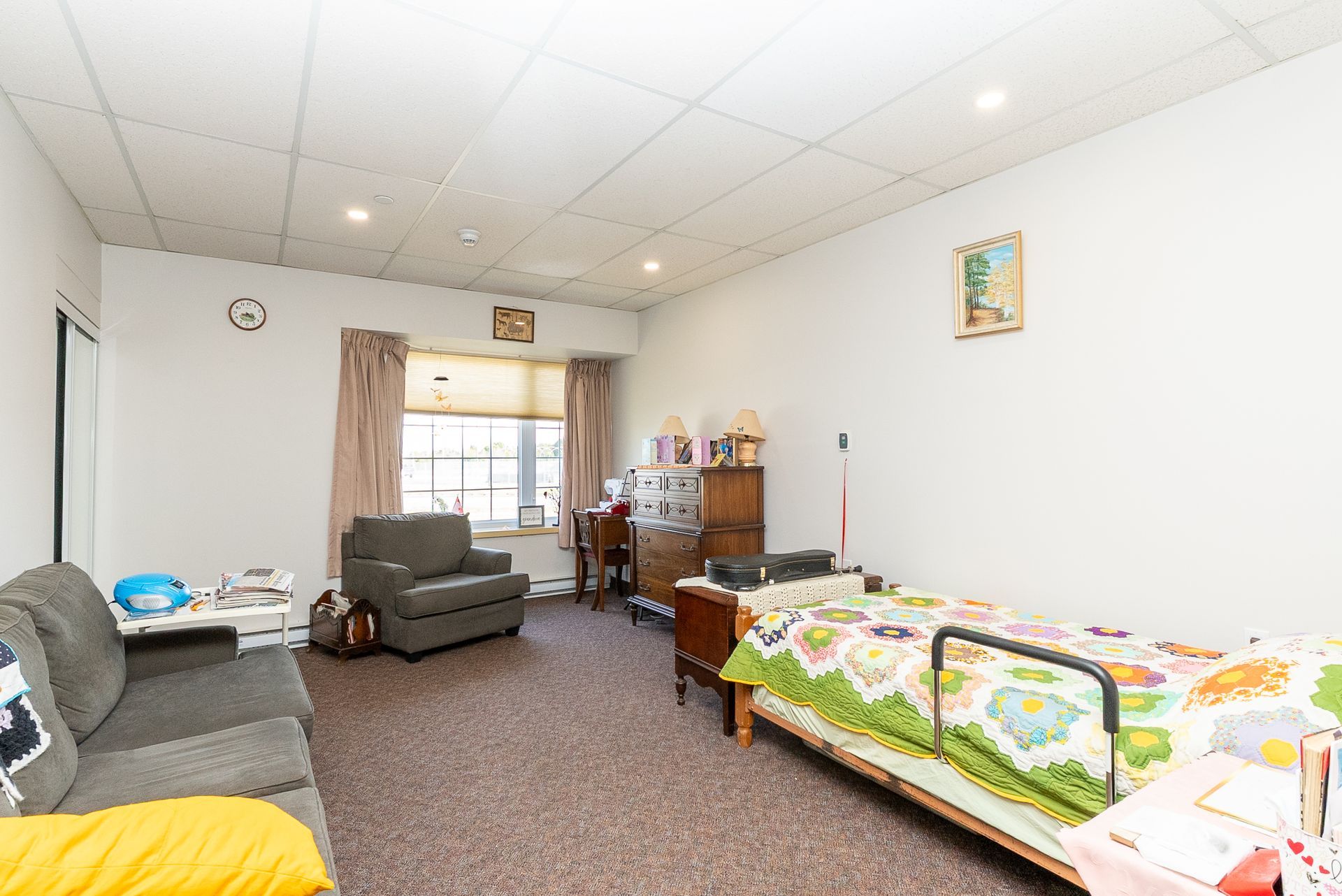 Living room with couches, armchair, window, and a child’s bed along the wall.
