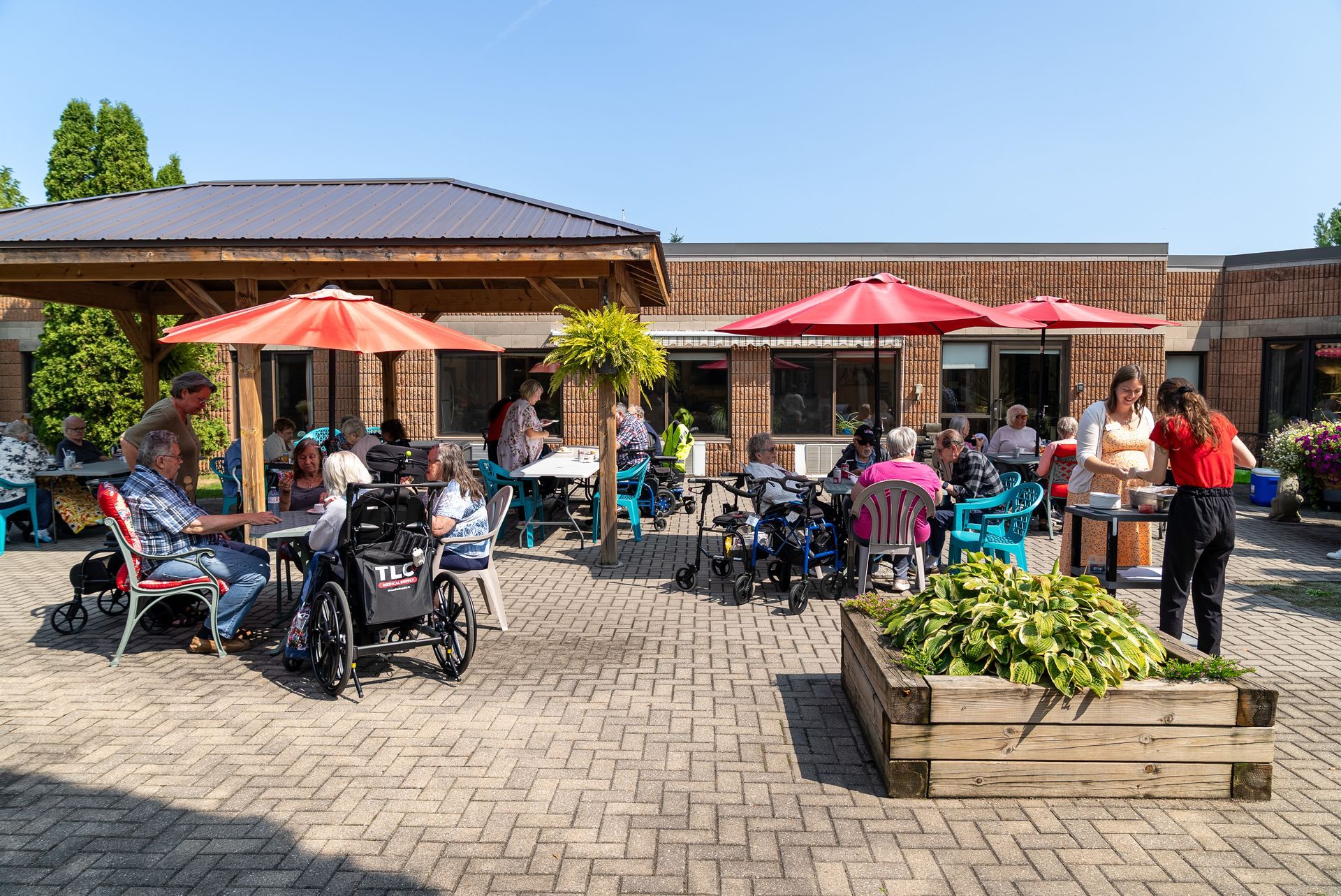 Outdoor café patio with red umbrellas, seated customers, and tables in bright sunlight