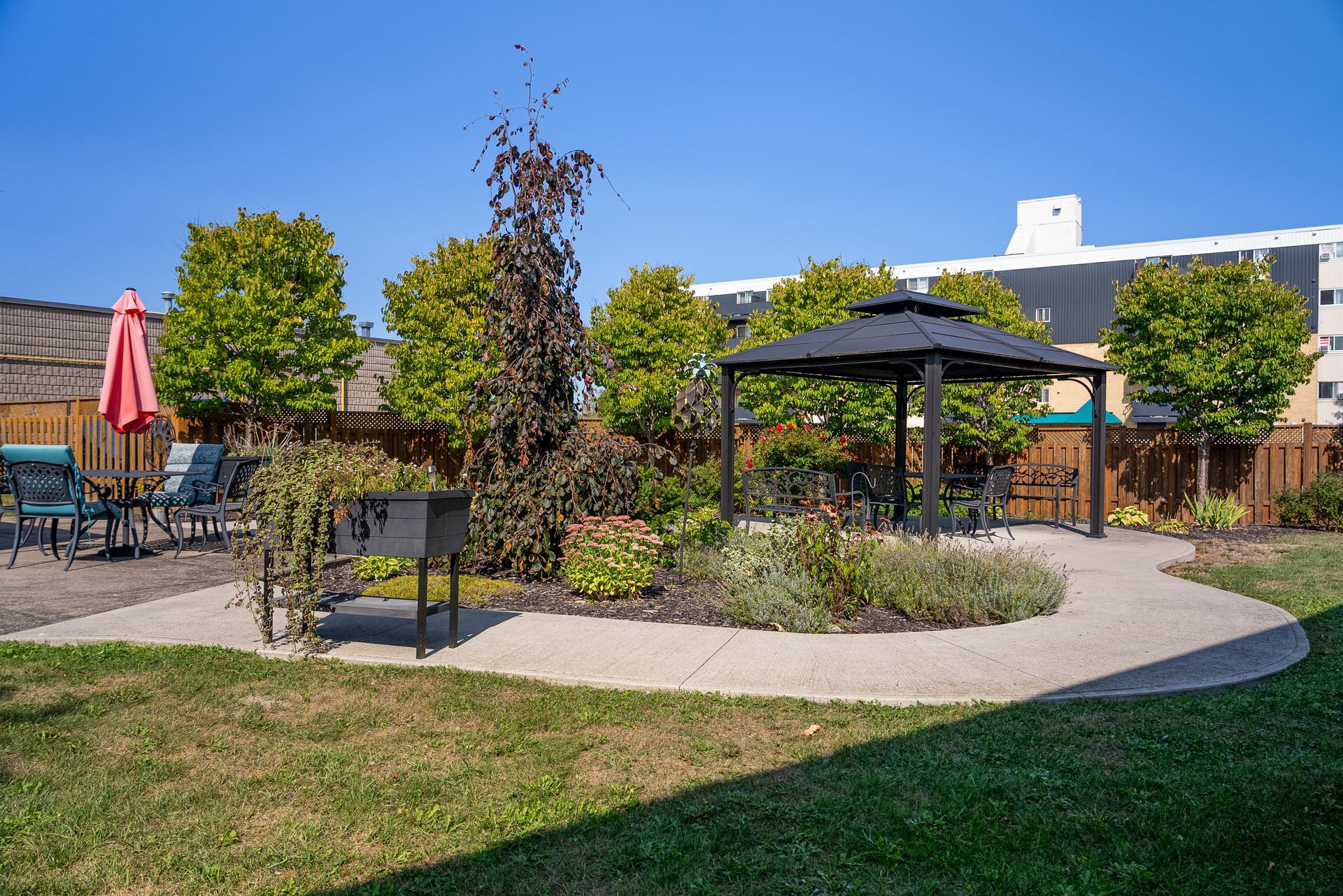Outdoor patio with gazebo, tables, chairs, and a red umbrella beside a grassy garden path