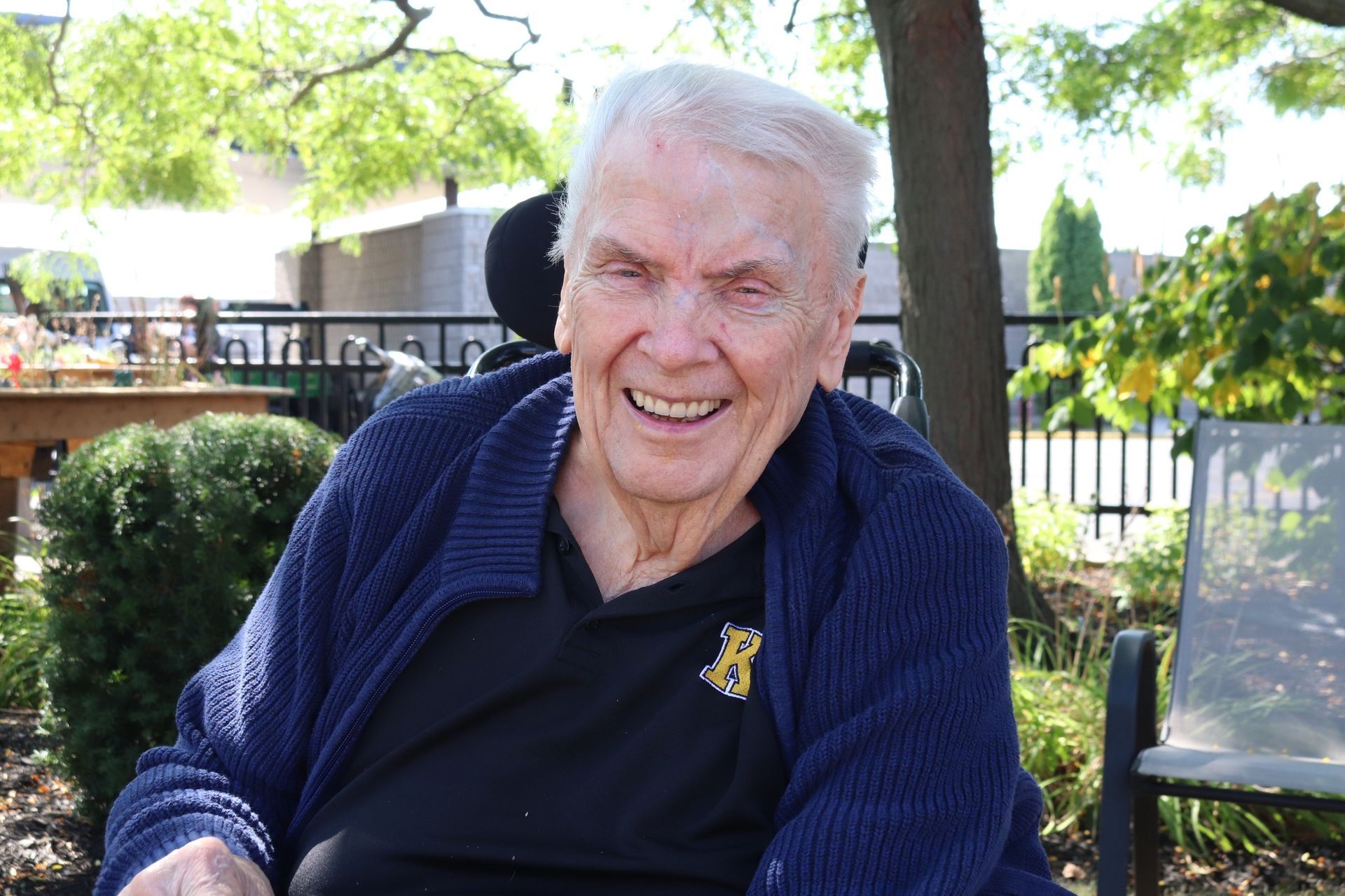 Smiling man in a navy cardigan sitting outdoors in a garden patio