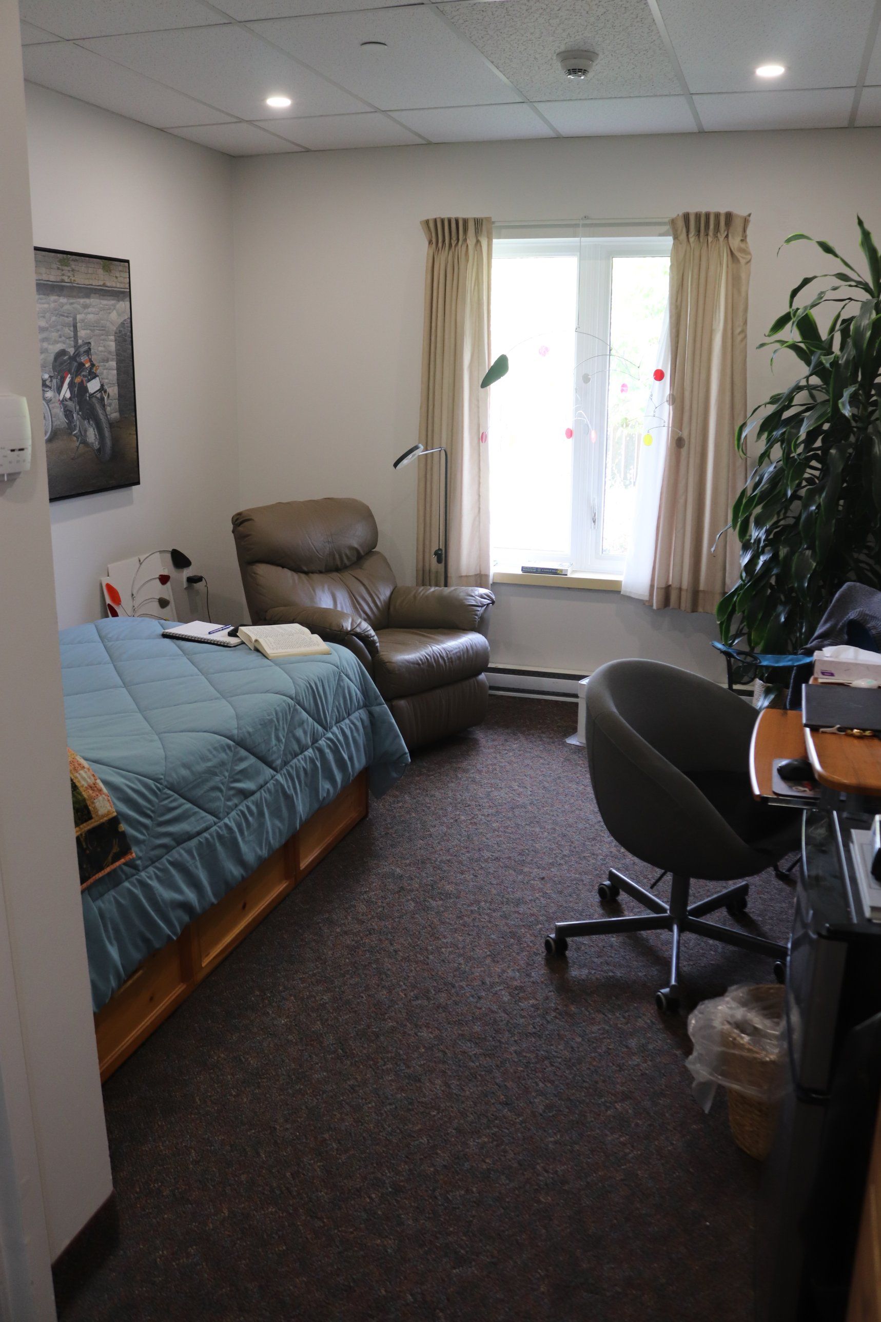 Standard lodge room with a bed, leather recliner, desk chair and a bright window with curtains