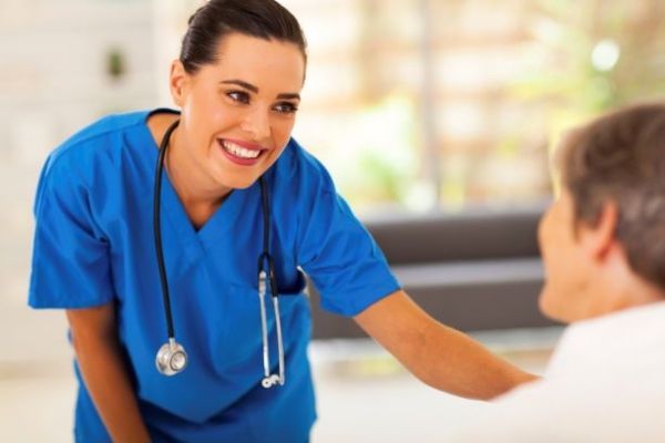 Smiling nurse in blue scrubs leaning toward a patient in a clinic room