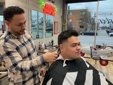 Barber trimming a client’s hair in a bright barbershop by the window.